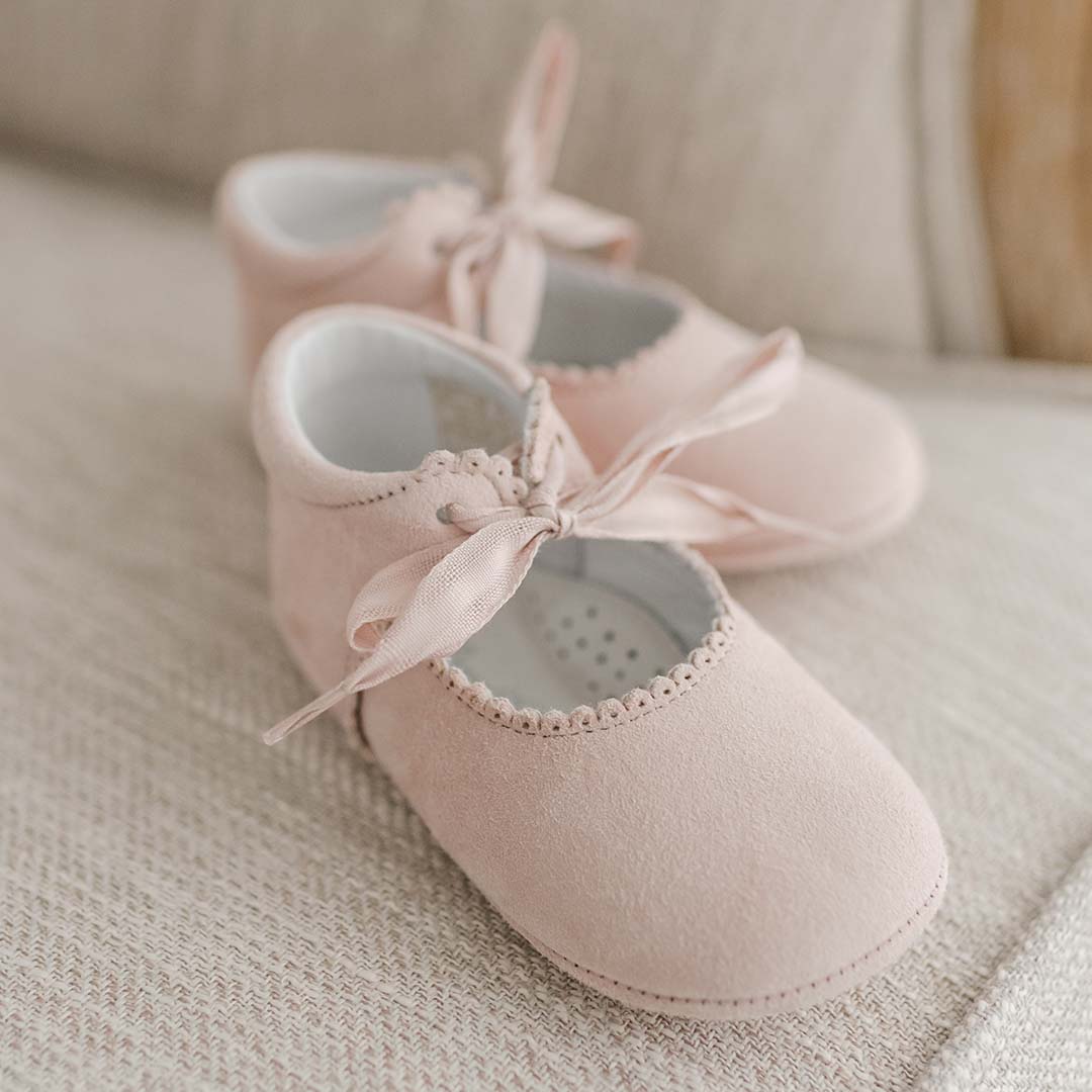 Flat lay of the Lola Suede Tie Mary Janes. The shoes are made from rosy bluish pink suede with scallop edge detailed and topped off with a soft cotton ribbon tie.