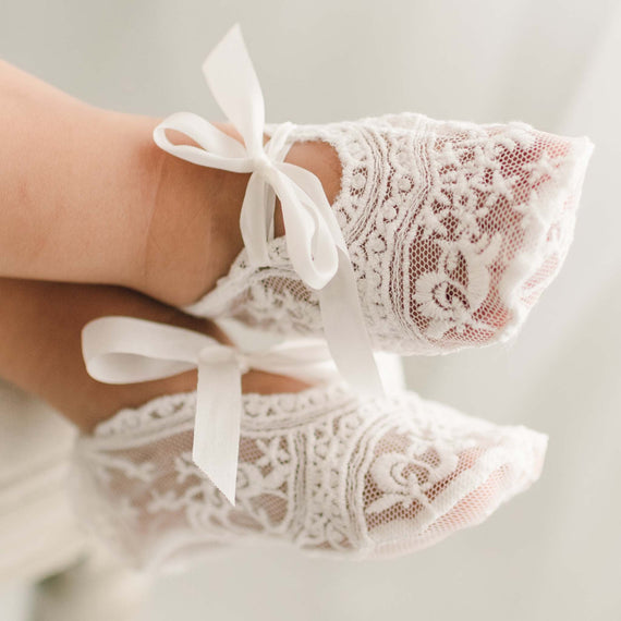 Light ivory sheer lace baby girl booties on feet.
