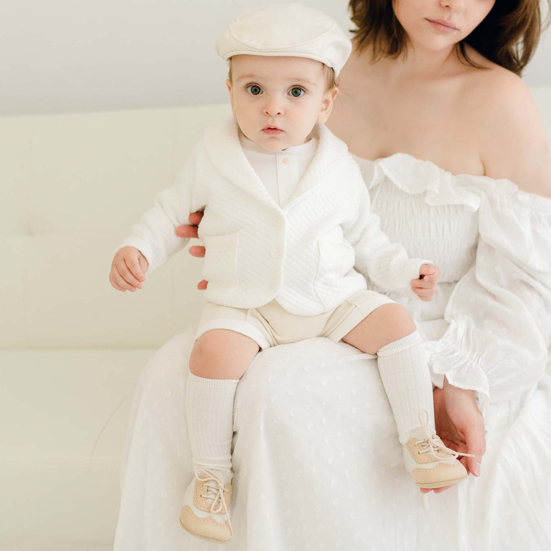 Baby boy sitting on his mother's lap. He is wearing the Braden 3-Piece Suit with the Newsboy Cap