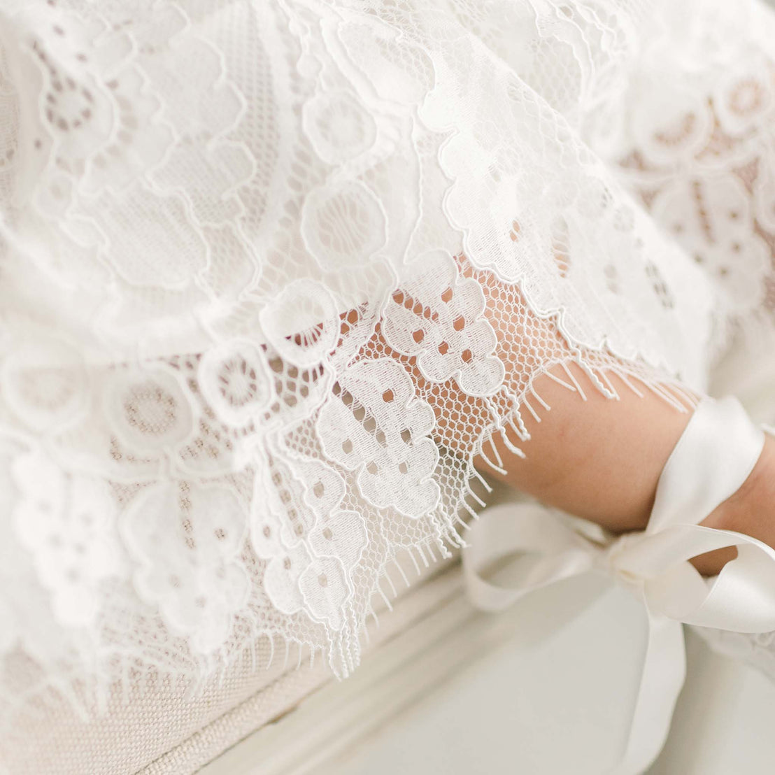 Detail of the ivory Victoria Puff Sleeve Christening Dress showcasing the embroidered ivory lace on the skirt.