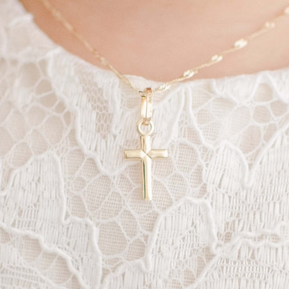 Tiny solid gold cross with tie detail on chain worn by baby