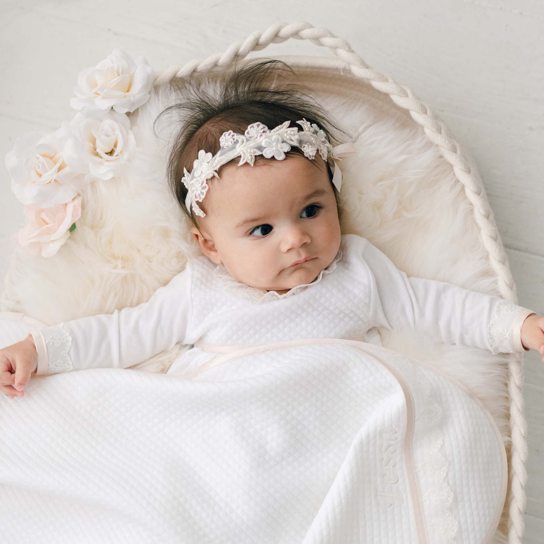 Newborn baby girl wearing the Tessa Flower Headband. The headband is accented with beautiful pink and white floral appliqué and a pink silk ribbon bow.