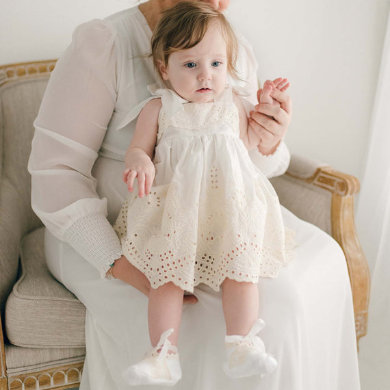 Baby girl sitting on her mother's lap and wearing an ivory Ingrid Romper Dress