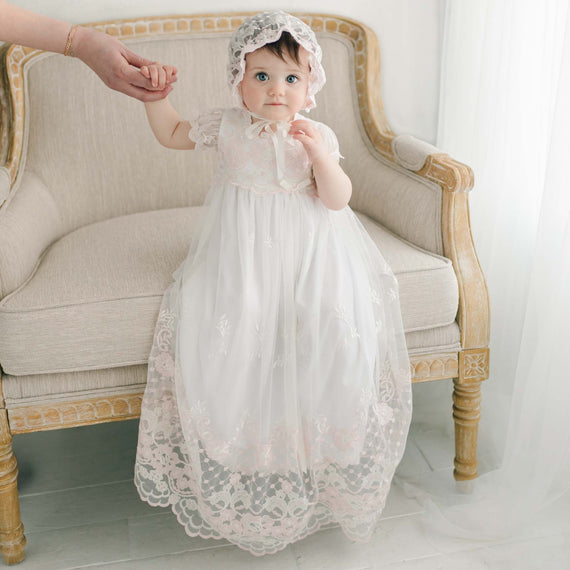 Baby girl sitting in pink and ivory baptism gown and bonnet