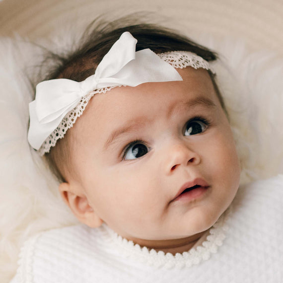 Newborn baby girl wearing the Tessa Lace Headband, which is made with from an elastic lace in Vintage Pink and finished with an Ivory silk ribbon bow.