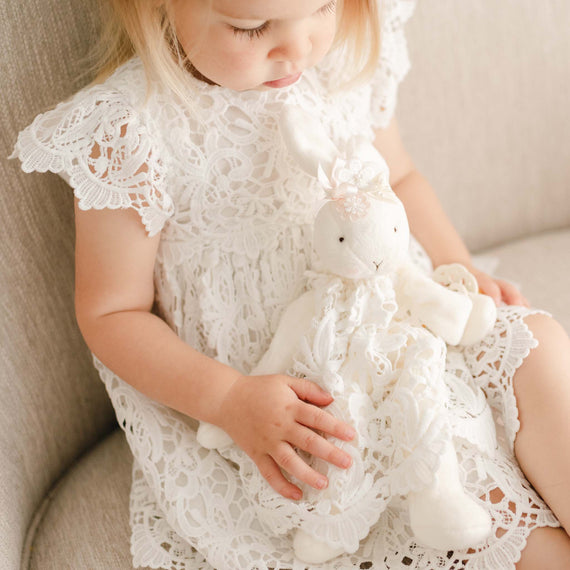 Baby girl wearing the Lola Dress. She is holding a Lola Silly Bunny Buddy pacifier holder with the same Lola Dress.