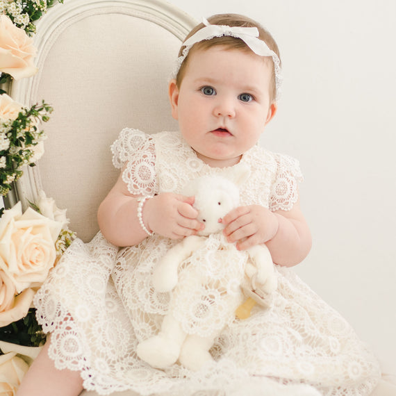Baby girl photographed in her christening dress with her plush lamb doll accessory.