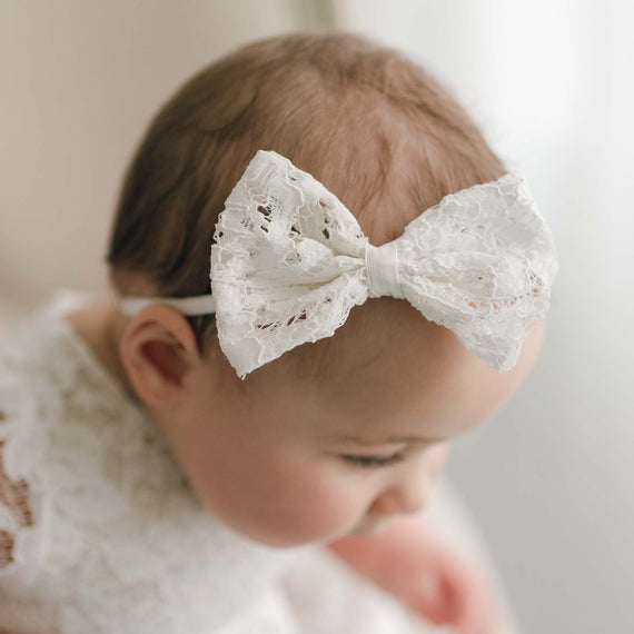 A close-up of a baby with a Rose Bow Headband, gazing downward. The baby's profile is softly illuminated by natural light, highlighting the delicate texture of the headband and the baby's features.