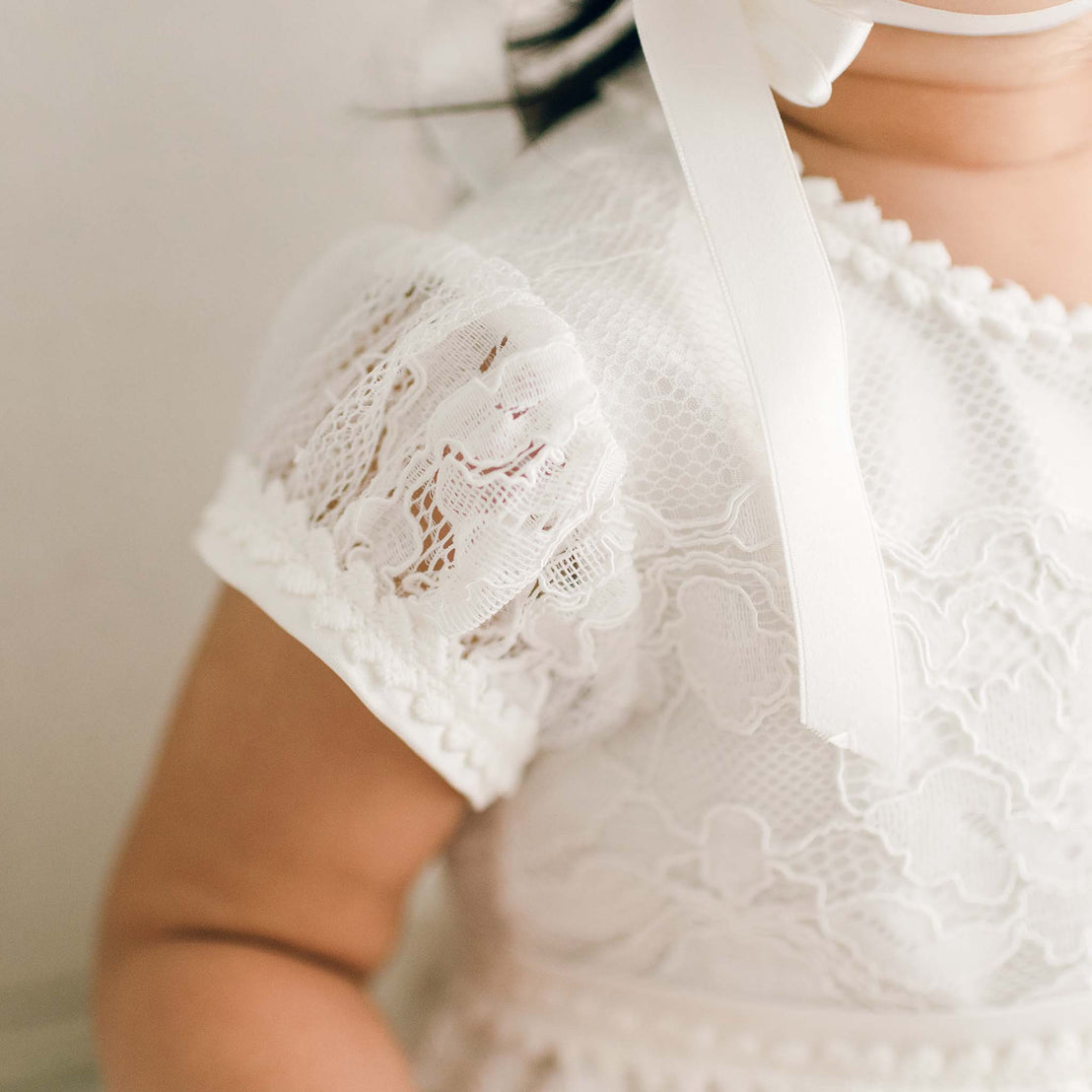 Detail of the ivory Victoria Puff Sleeve Christening Dress showcasing the embroidered ivory lace on the sleeve.