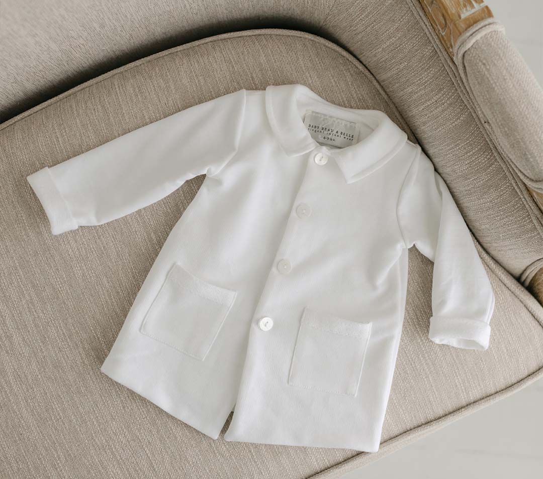 Flat lay photo of the Miles Trench Coat on a chair. It is made of white french terry cotton with buttons and pocket details