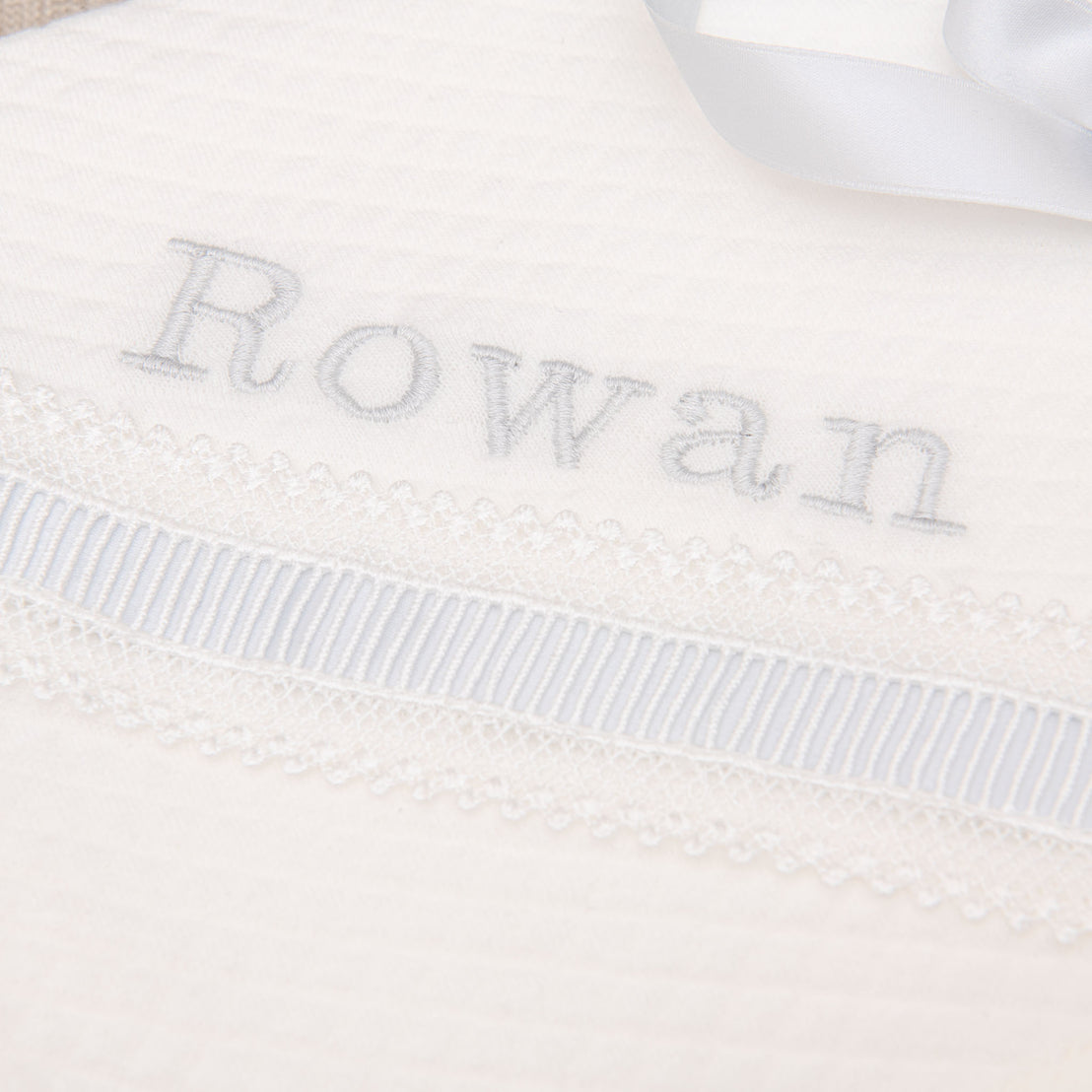 Close up detail of silk embroidery and name 'Ronan' personalized on baptism blanket.