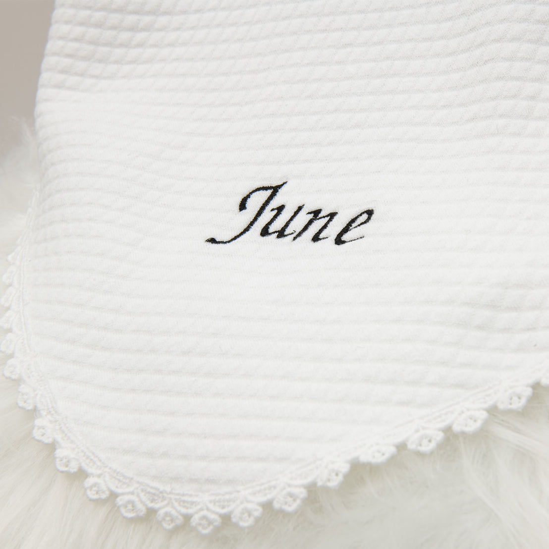 Close-up of a June Personalized Blanket with a scalloped lace edge, featuring the word "june" embroidered in black cursive script after a christening.