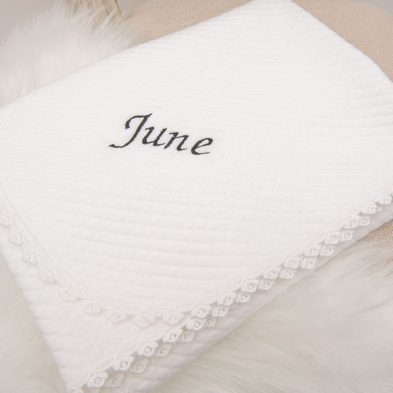 Stylish white June Personalized Blanket with lace trim and the name "June" embroidered in black cursive script, positioned on a soft beige surface.