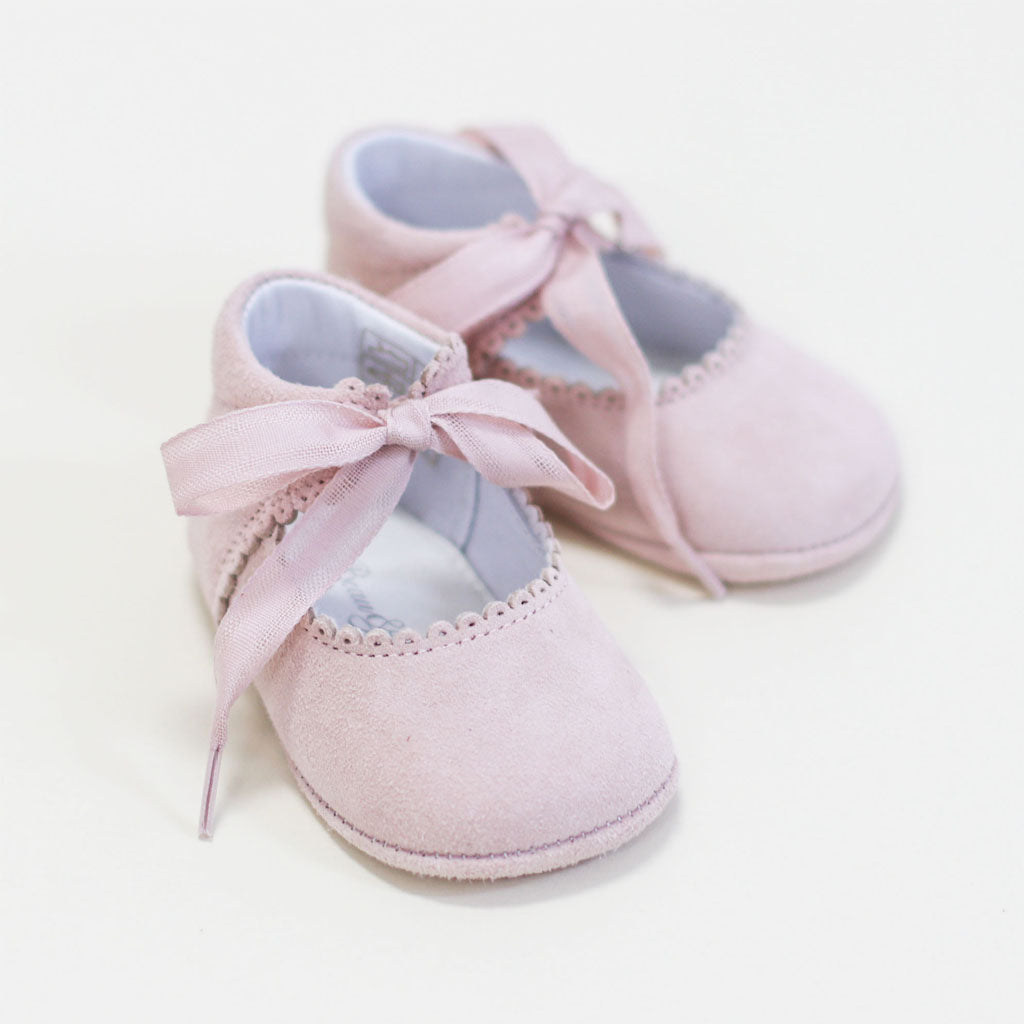A pair of stylish pink baby June Suede Tie Mary Janes with ribbon ties on a white background, perfect for after the christening.