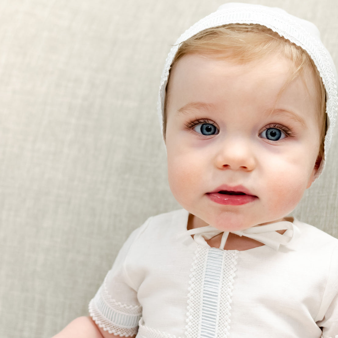 Baby boy looking into camera wearing a traditional boys bonnet.