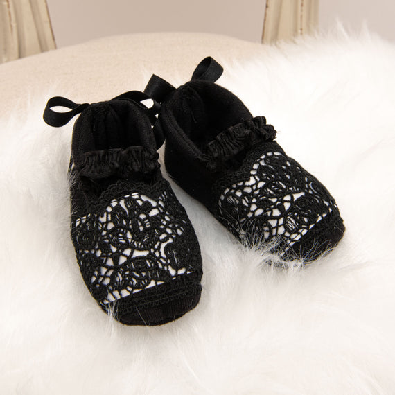 A pair of stylish black lace June Booties with ribbon ties, placed on a soft white furry surface.