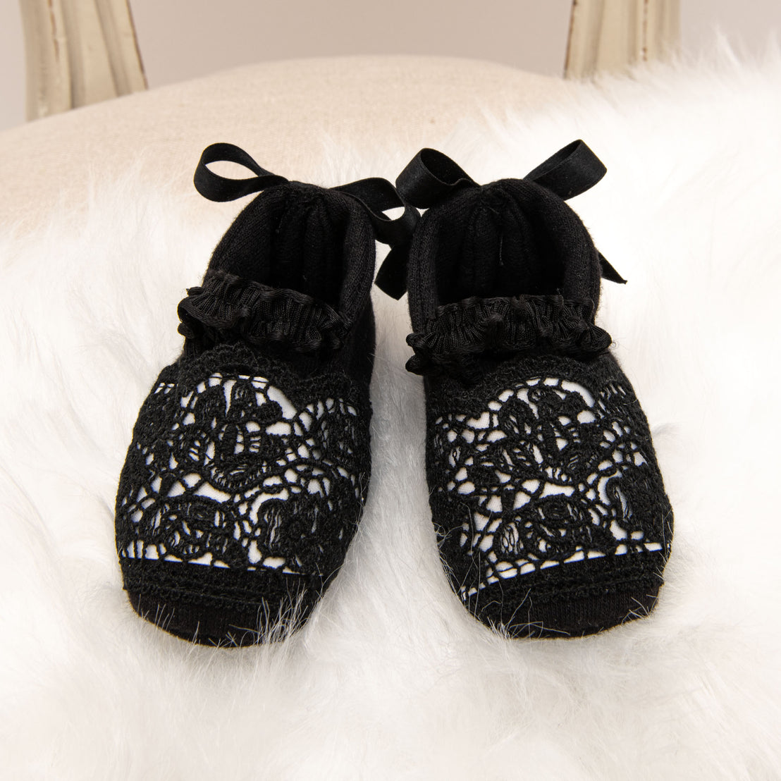 A pair of stylish black June Booties with ribbon ties, displayed on a fluffy white surface.