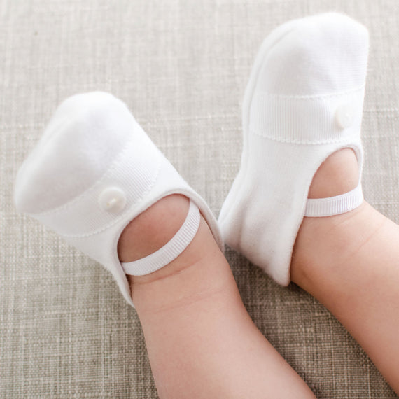 Baby wearing the Elliott Booties made from white French terry and featuring grosgrain ribbon detailing across the toe with a button. 
