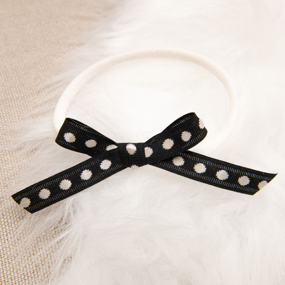 A stylish June Bow Headband with white polka dots tied into a bow, set against a white fluffy background.