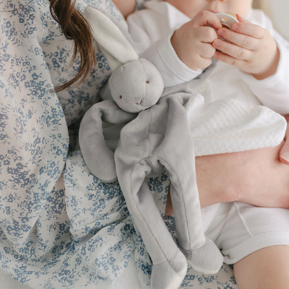 Baby boy with his mother. He is holding onto the Miles Silly Bunny Pacifier Holder, a grey bunny stuffed animal