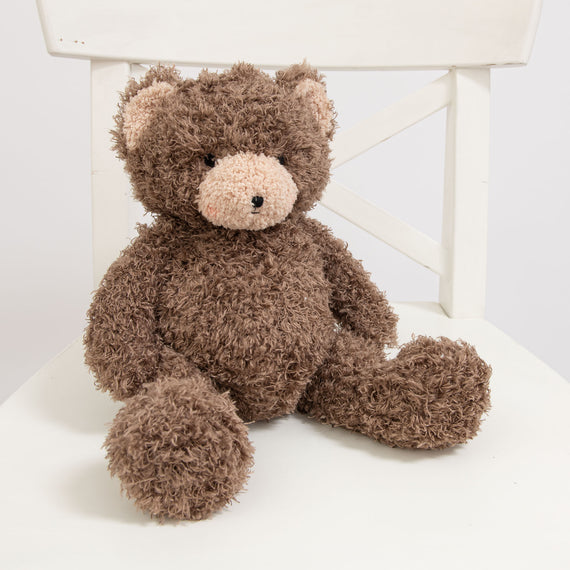 A photo of the Cubby Bear, a soft stuffed animal bear, sitting on a white chair.