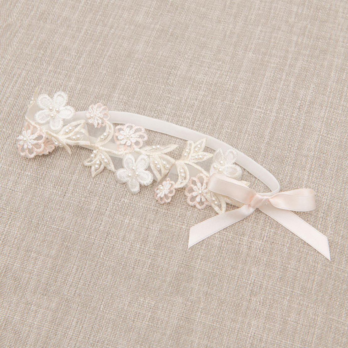 Flat lay photo of the Tessa Flower Headband. The headband is accented with beautiful pink and white floral appliqué and a pink silk ribbon bow.