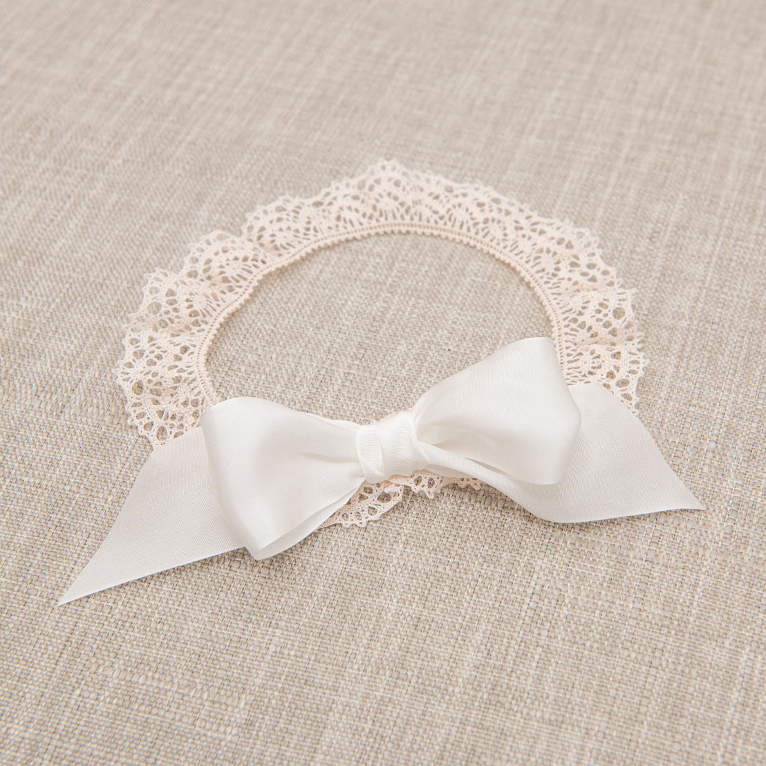 Flat lay photo of the Tessa Lace Headband, which is made with from an elastic lace in Vintage Pink and finished with an Ivory silk ribbon bow.