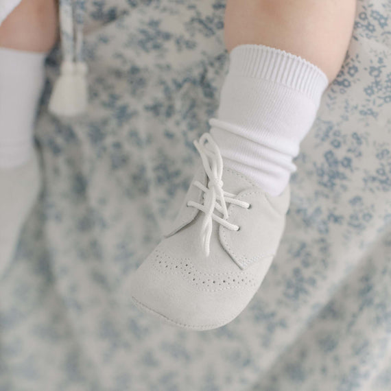 Photo of a baby foot wearing the Miles Suede Shoes. Made with a soft grey suede with detailed edging.