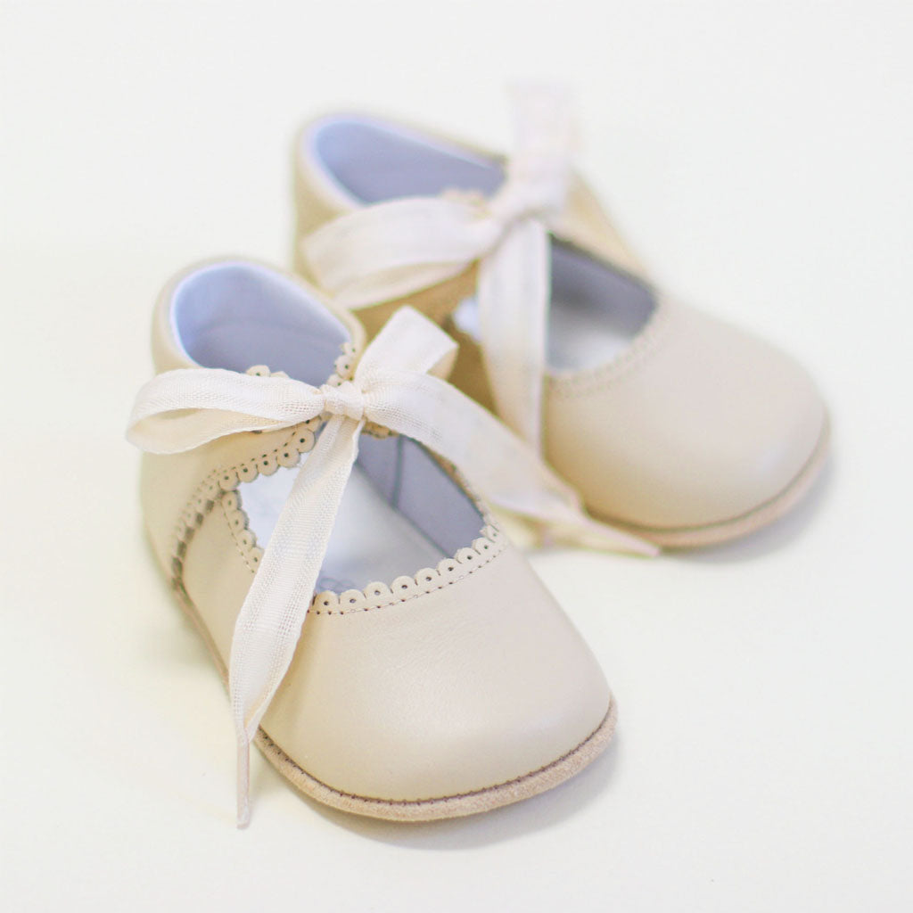 A flat lay photo of the Tan Tie Mary Janes crafted with tan matte leather with beautiful scallop edge detail and complimenting cotton ribbon tie