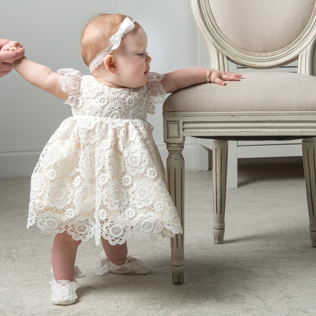 Poppy Blessing Dress & Bonnet. Baby girl standing next to chair.
