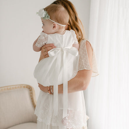 A godmother holding her goddaughter in a baptism dress with a long silk bow