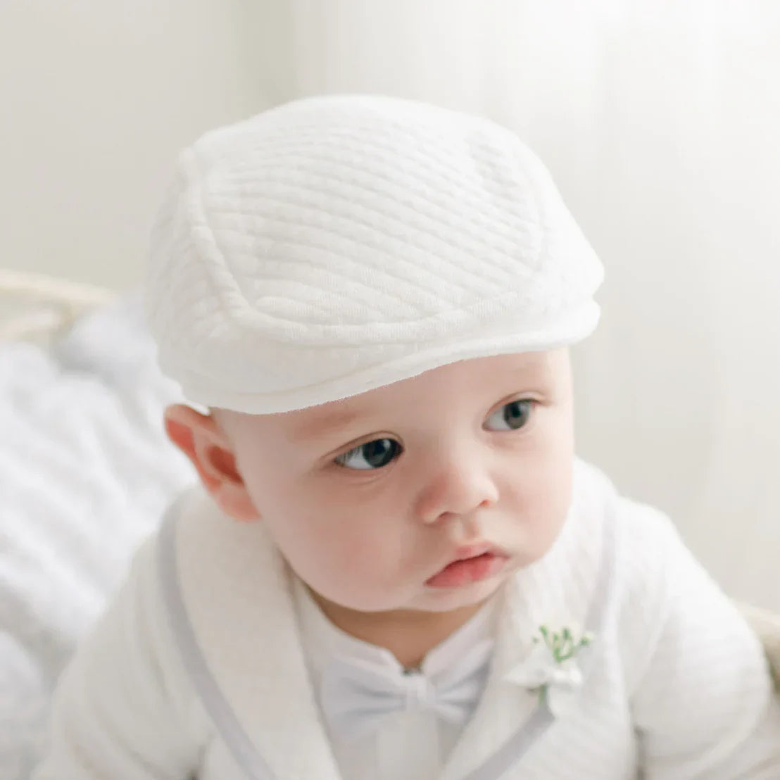 A closeup of a boys face wearing the Harrison christening suit featuring a quilted newsboy cap. 