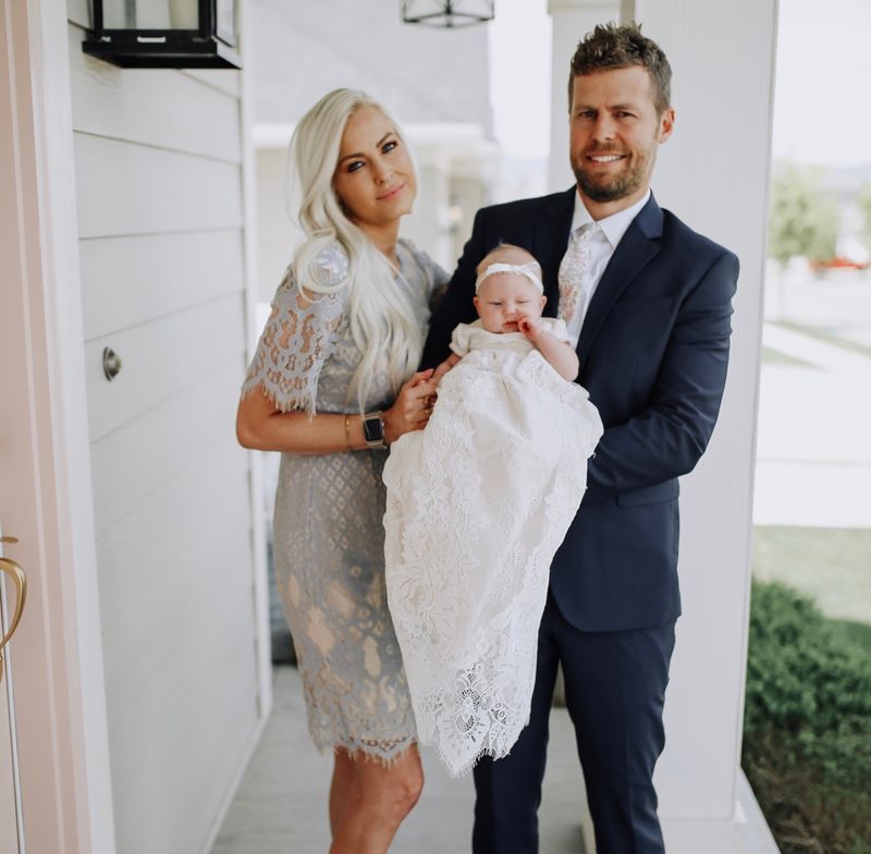 a couple holding their baby in a christening gown