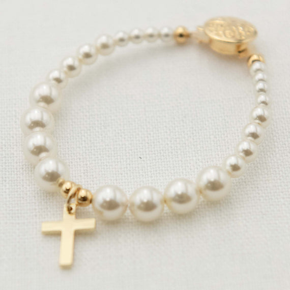 Pearl bracelet with a gold cross charm on a neutral background