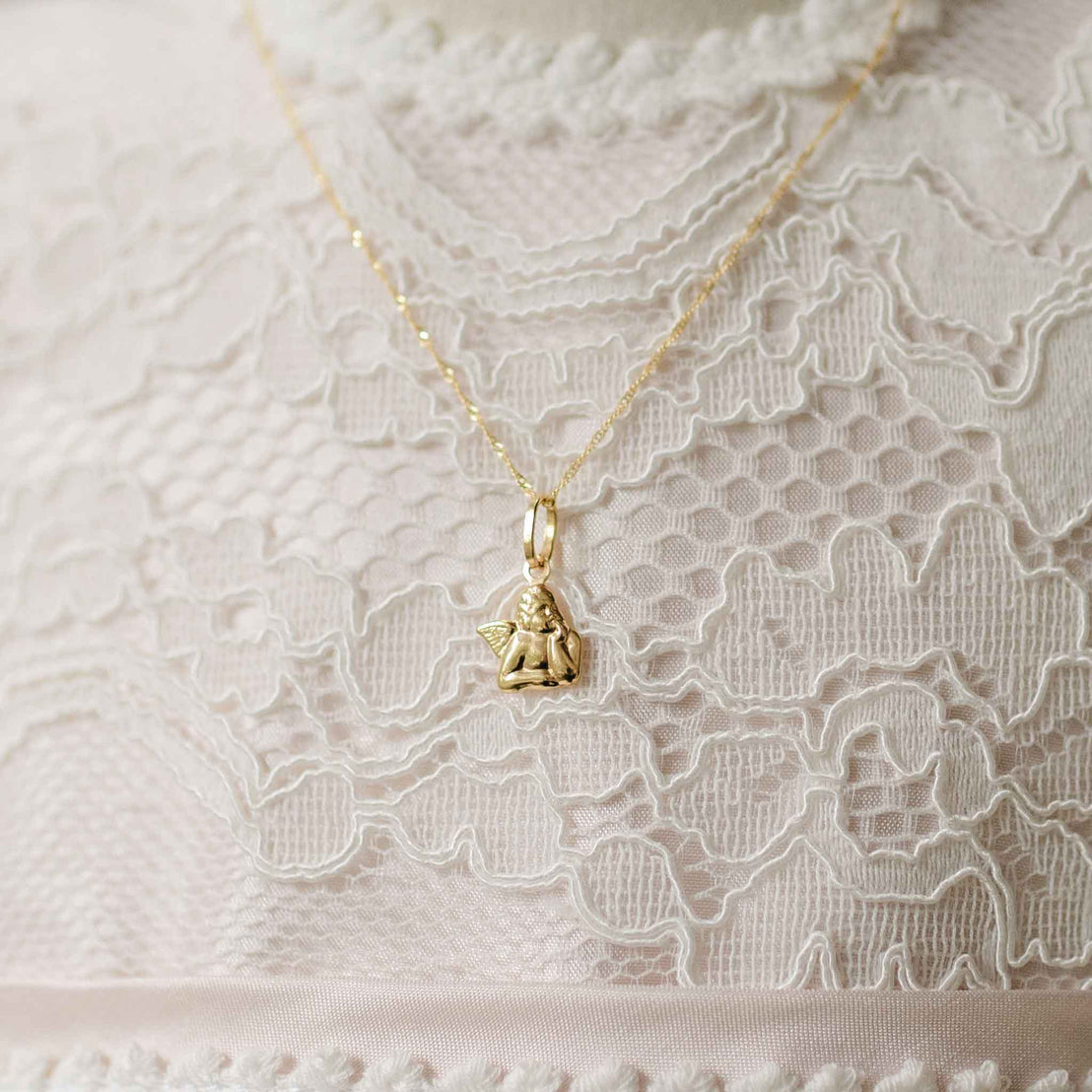 Gold necklace with a small angel pendant on a lace fabric background