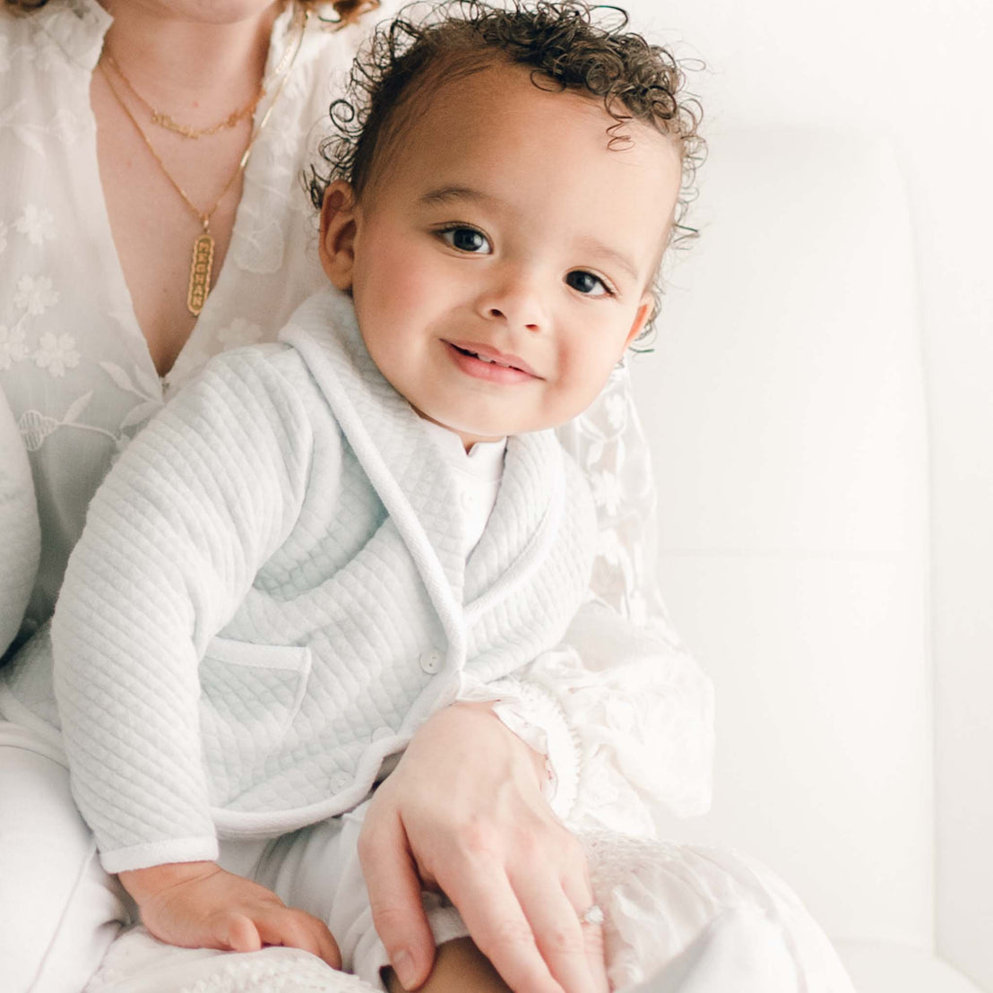 Close up detail of a baby boy (with his mother) wearing the powder blue Asher 3-Piece Suit, including a folded collar jacket, white pants and a onesie with buttons (and matching Quilted Newsboy Cap). 