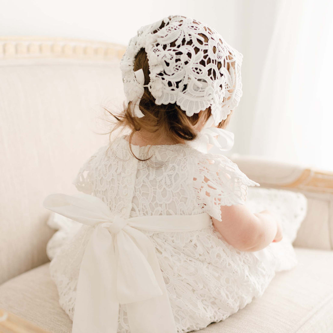 Detail of the back of the Lola Christening Gown and Bonnet. The gown is worn by a baby girl and the detail shows the ties in back with a cotton sash and button closure.