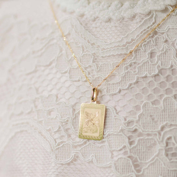 Gold necklace with a rectangular pendant on a lace background
