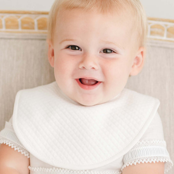 Baby boy smiling wearing the Rowan baptism bib, made of quilted white cotton.