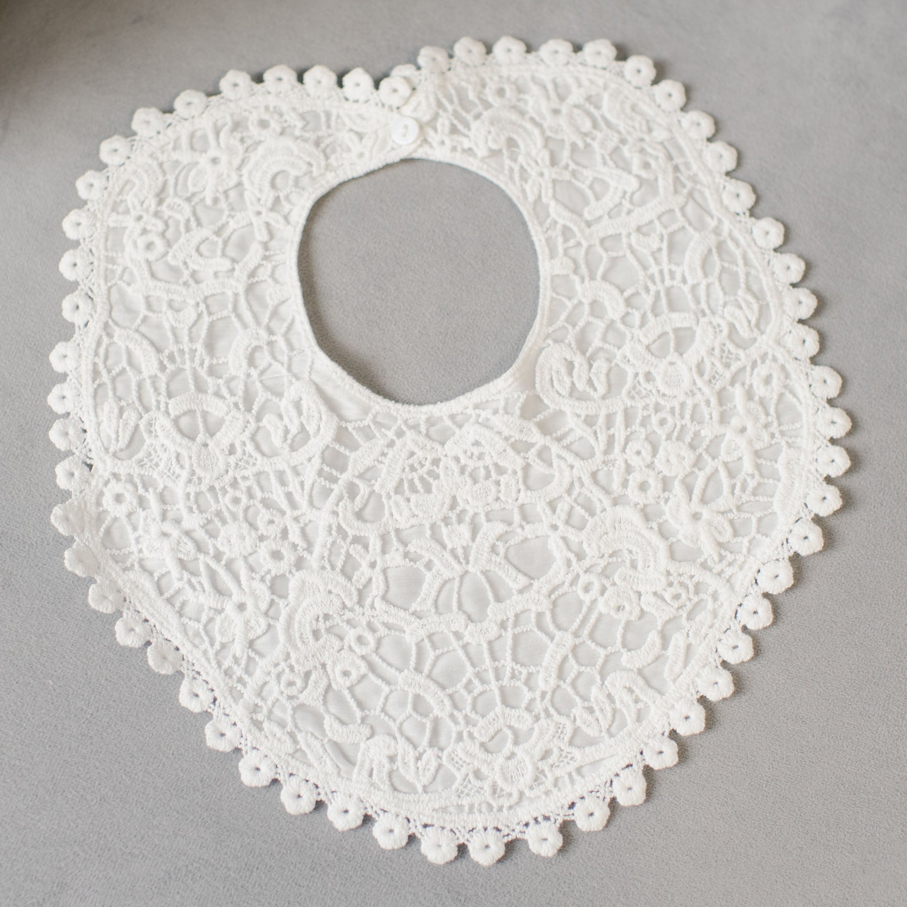 A white lace baby bib featuring intricate floral patterns and scalloped edges is elegantly displayed on a gray surface, perfectly complementing the Grace Accessory Bundle - Save 15%.