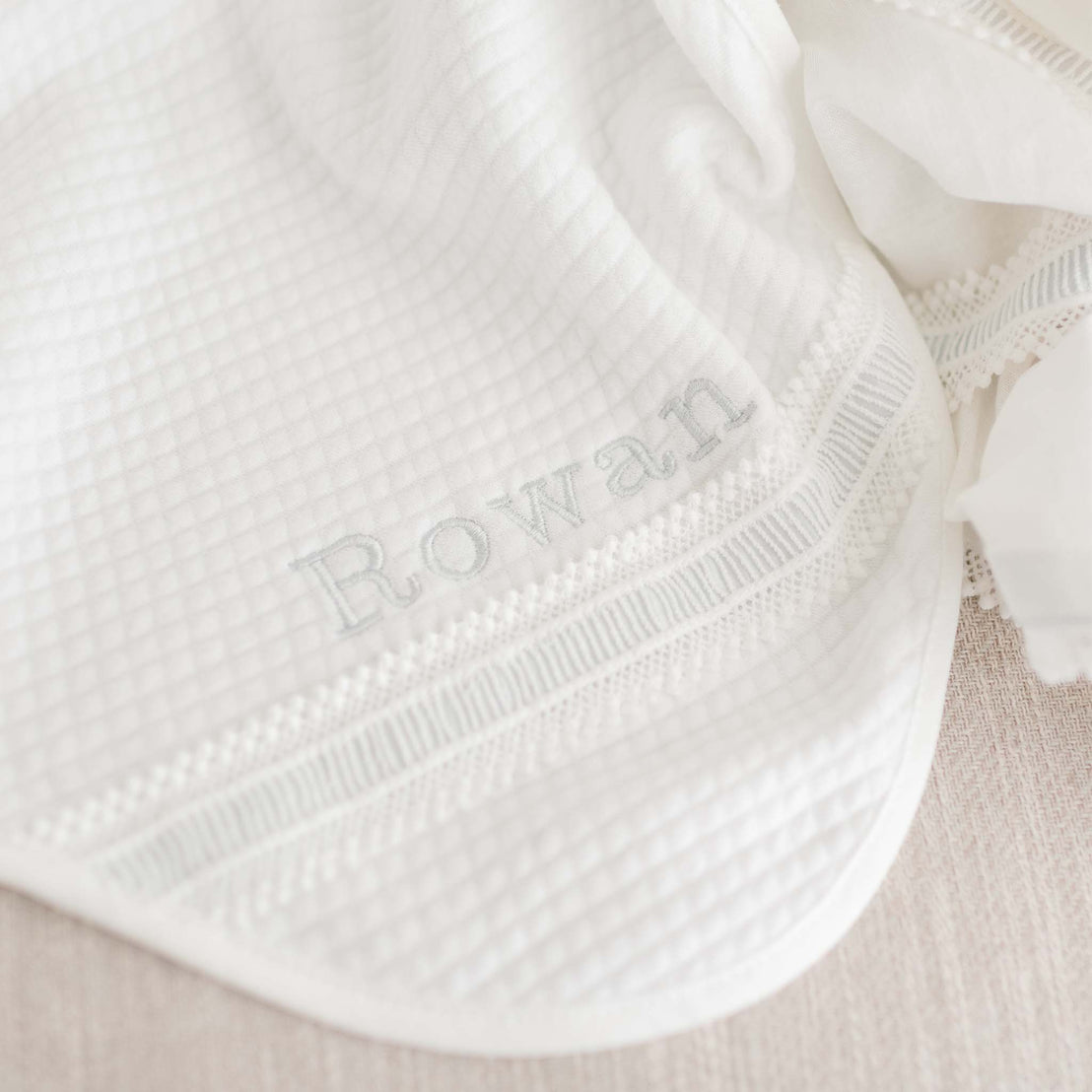 Close up detail of name 'Rowan' in silk embroidery on the personalized baby boy baptism blanket. 