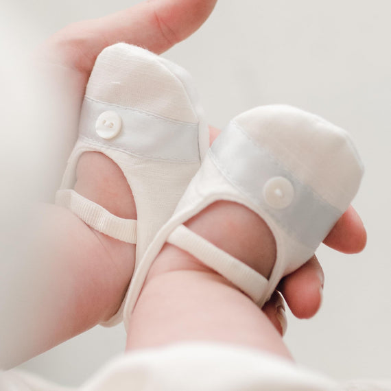 Photo of baby wearing the Owen Linen Booties made from a soft cotton and detailed with a blue silk ribbon and button on top