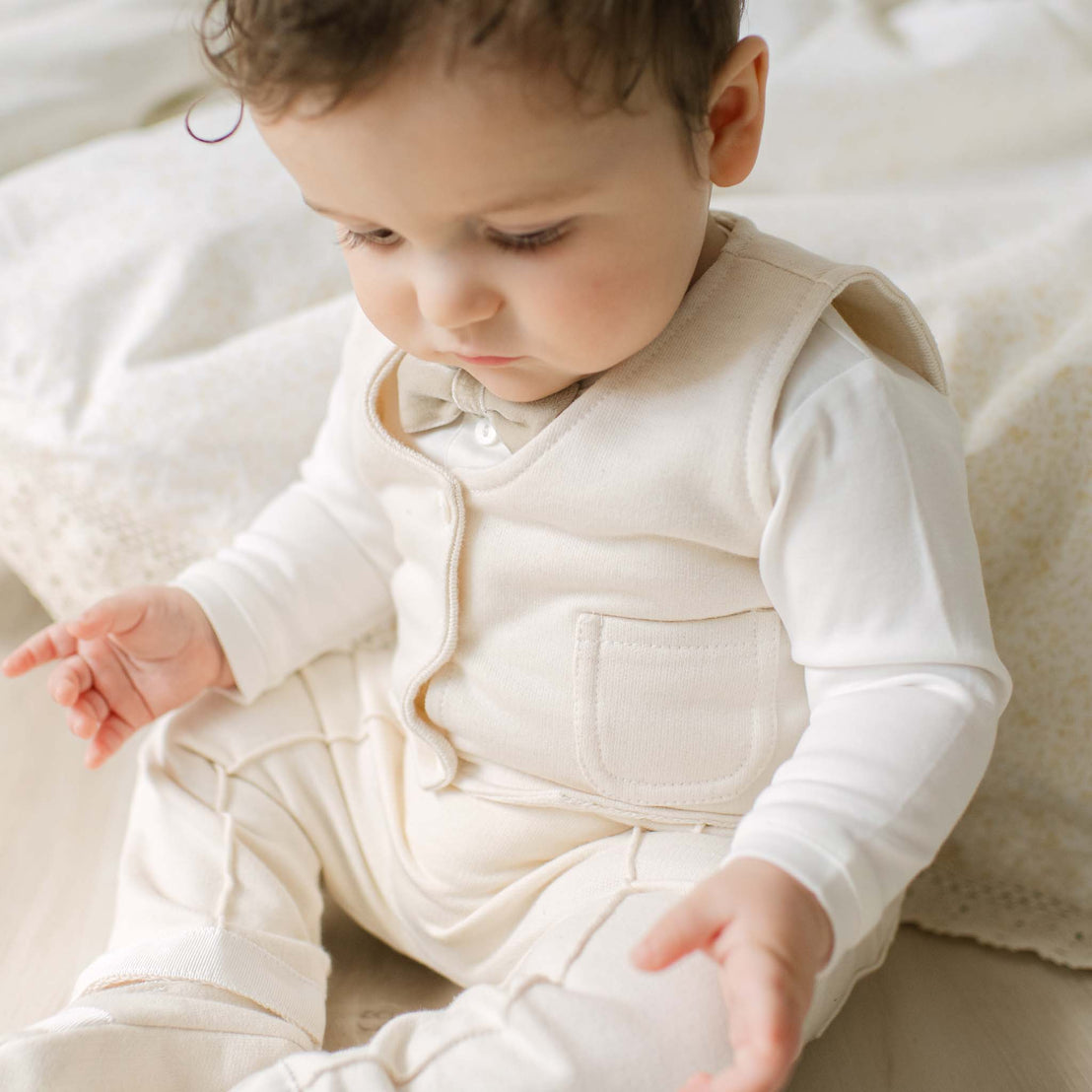 Baby wearing a cream-colored outfit sitting on a soft surface