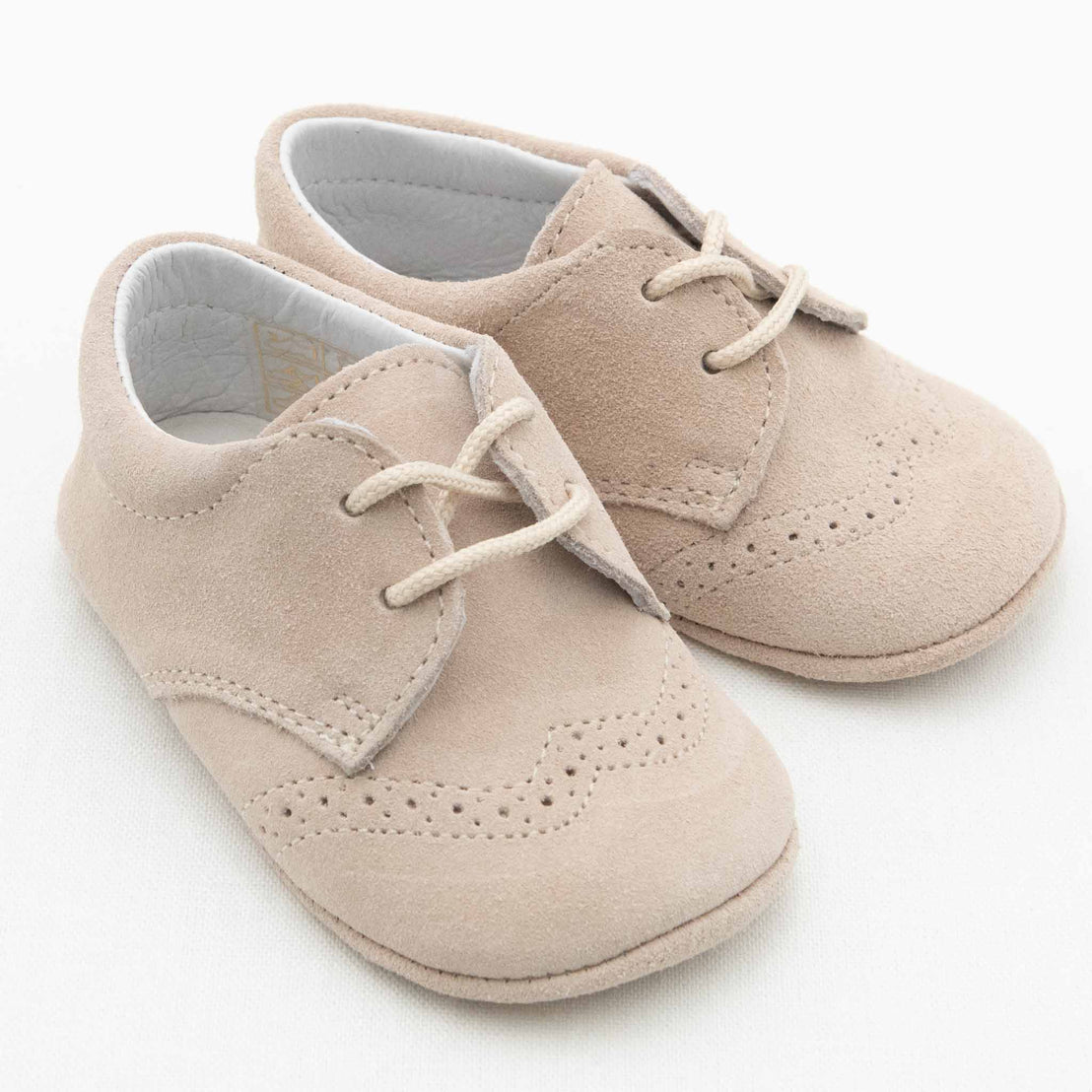 A pair of Camel Suede Shoes from Baby Beau & Belle, designed for boys with laces and intricate decorative stitching details. These shoes, with their handcrafted appearance, are made from a soft suede-like material and are set against a plain white background.