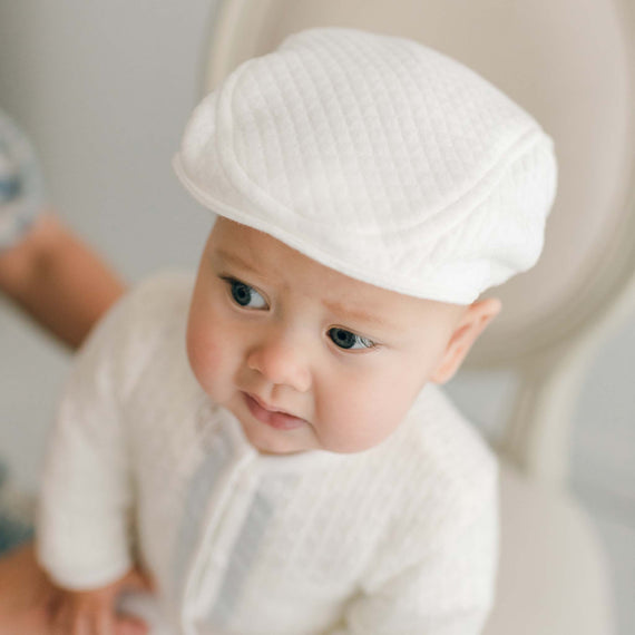 Baby boy sitting on a chair and wearing the Owen Cotton Newsboy Cap made with ivory quilted cotton