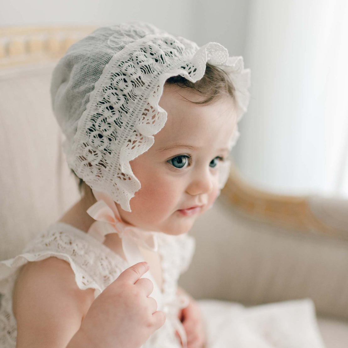 Close-up of a baby girl wearing a delicate white Charlotte Christening Gown & Bonnet with rose and vine embroidery, focusing on the texture of the cotton lace.