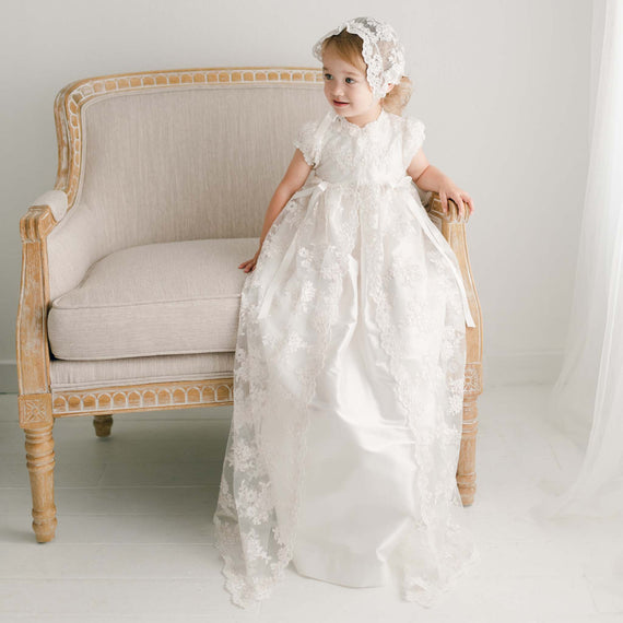Baby girl sitting in chair wearing an heirloom Christening Gown made of luxurious silk and lace netting. 