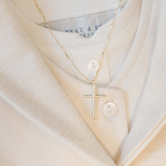The 14k Gold Cylindrical 'INRI' Cross Charm With Chain is elegantly showcased against a cream-colored, buttoned-down shirt.