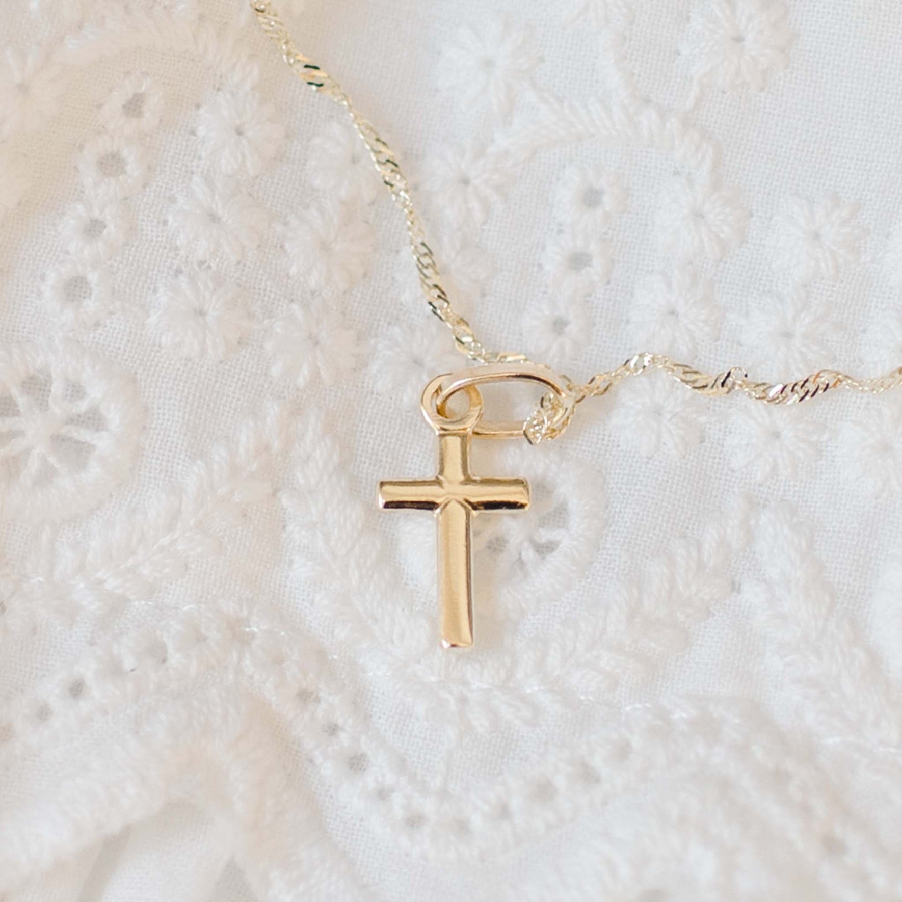 Small solid gold cross on chain with lace background