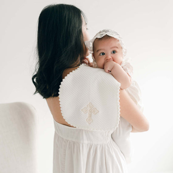 Woman holding a baby with a blanket embroidered with a cross design draped across her shoulder